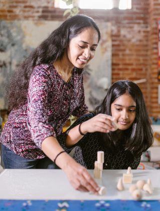 A mother and daughter enjoy creative play with wooden blocks indoors, enhancing family bonding and learning.